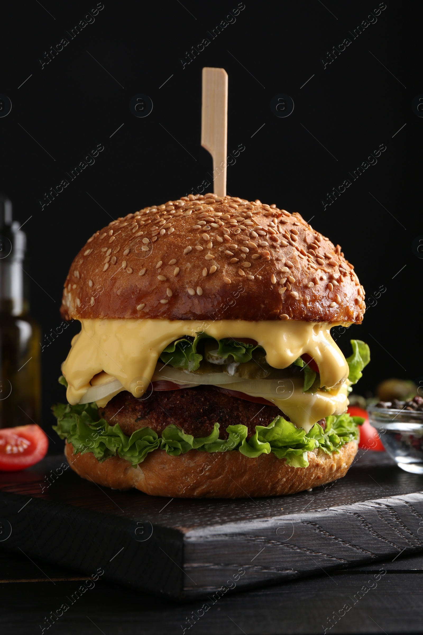 Photo of Vegetarian burger with delicious patty and cheese on black wooden table