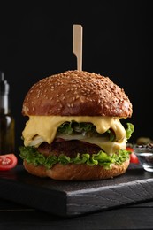 Photo of Vegetarian burger with delicious patty and cheese on black wooden table