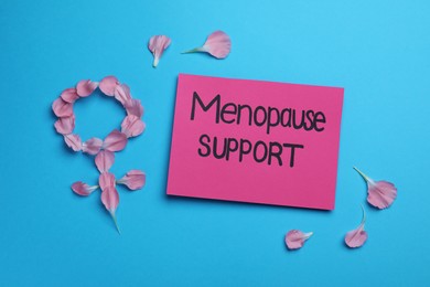 Photo of Note with words Menopause Support and female gender sign made of petals on light blue background, flat lay