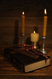 Photo of Church candles, cross, Bible and rosary beads on wooden table
