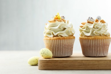 Tasty Easter cupcakes with vanilla cream and candies on gray table, space for text