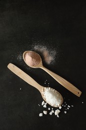 Photo of Different types of organic salt in spoons on black table, flat lay