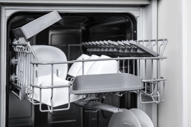 Photo of Open modern dishwasher with clean tableware, closeup
