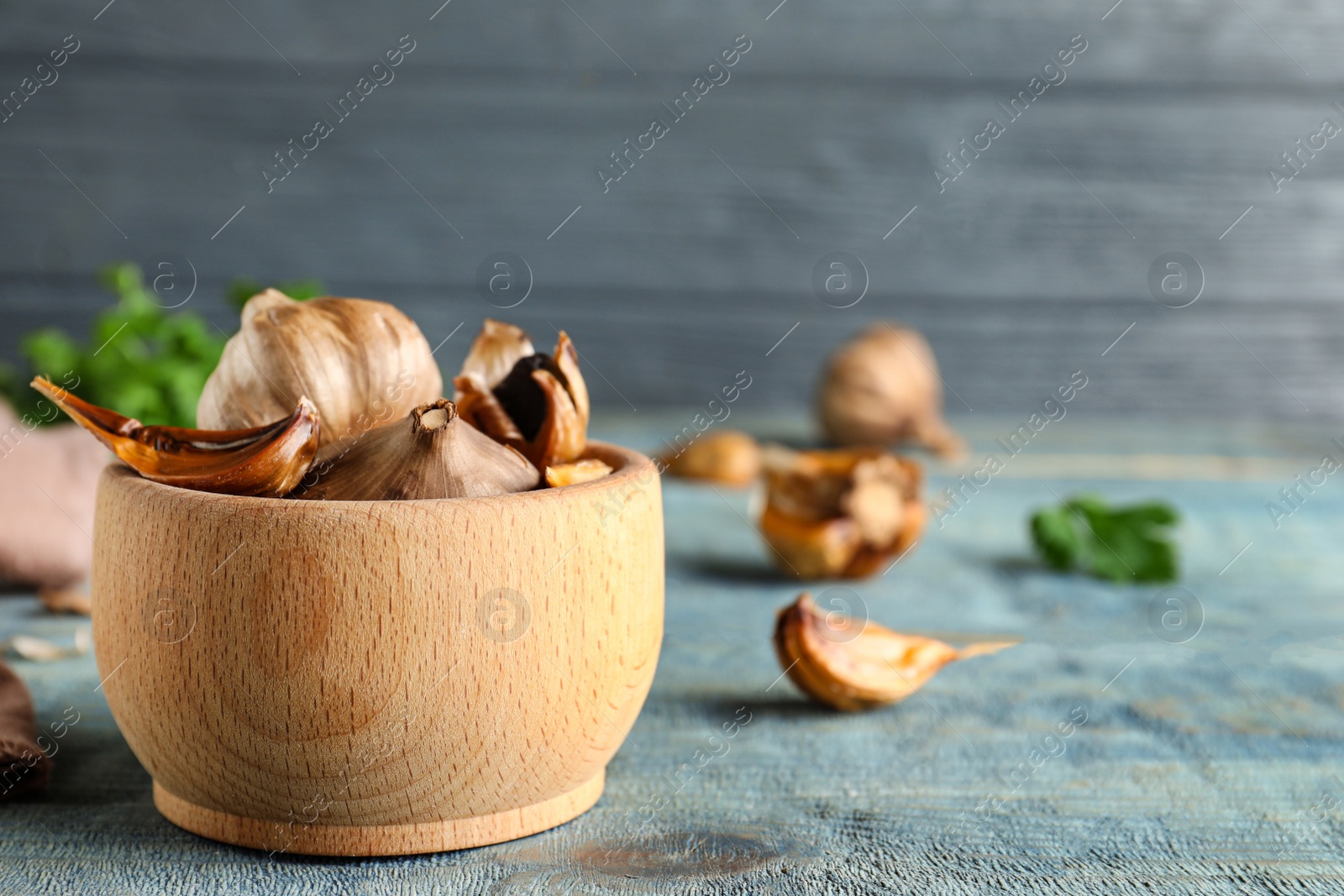 Photo of Bowl of black garlic on blue wooden table. Space for text