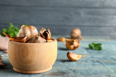 Photo of Bowl of black garlic on blue wooden table. Space for text