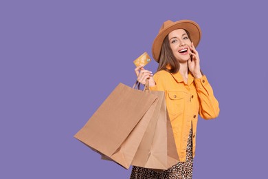 Photo of Stylish young woman with shopping bags and credit card on purple background. Space for text