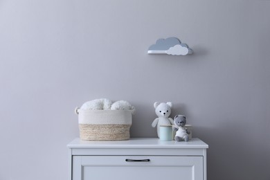 Child's toys, wicker basket and accessories on chest of drawers near light grey wall indoors