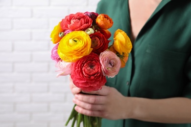 Woman holding beautiful ranunculus flowers near white brick wall, closeup