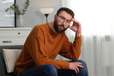 Overwhelmed man in glasses sitting on sofa at home