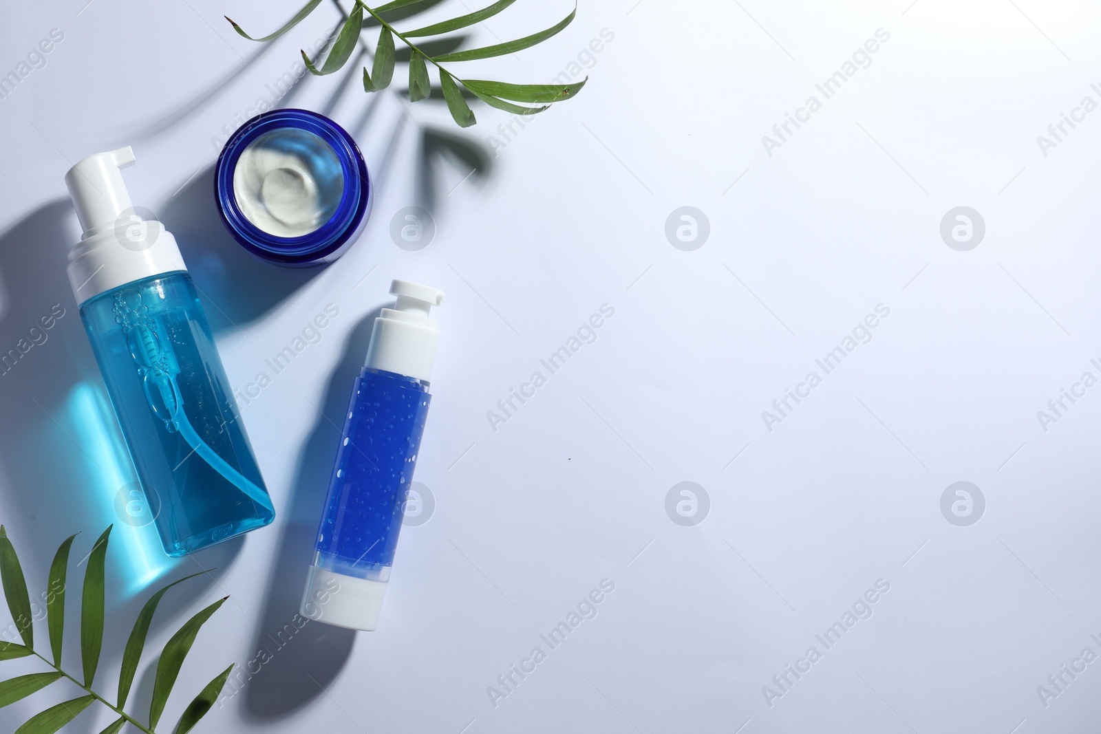 Photo of Set of cosmetic products and green leaves on white background, flat lay. Space for text