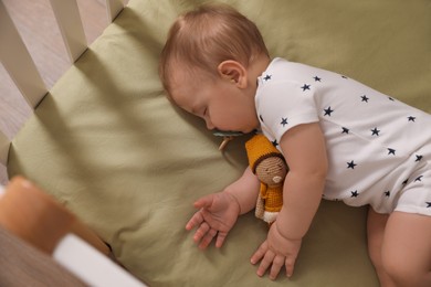 Photo of Adorable little baby with pacifier and toy sleeping in crib, above view