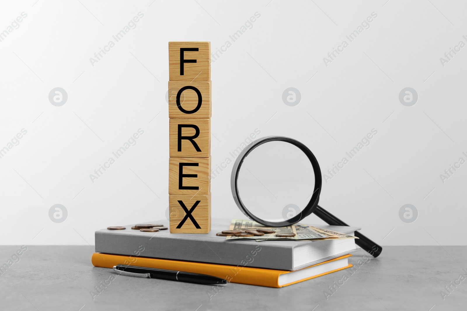 Photo of Word Forex made of wooden cubes with letters, magnifying glass and notebooks on light grey table