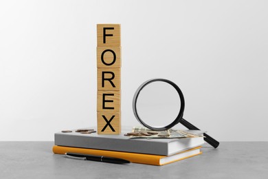 Photo of Word Forex made of wooden cubes with letters, magnifying glass and notebooks on light grey table