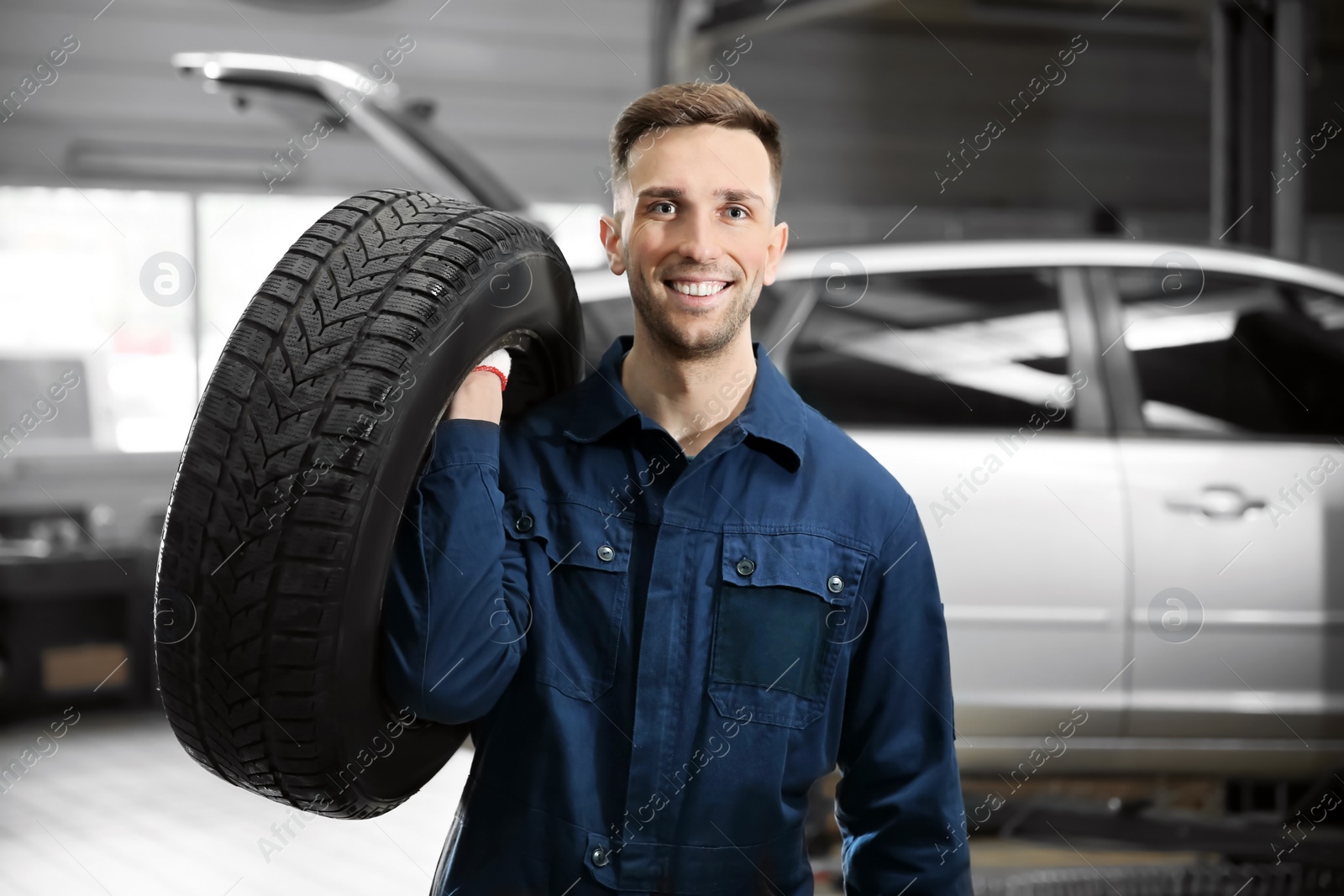 Photo of Young mechanic with car tire in service center