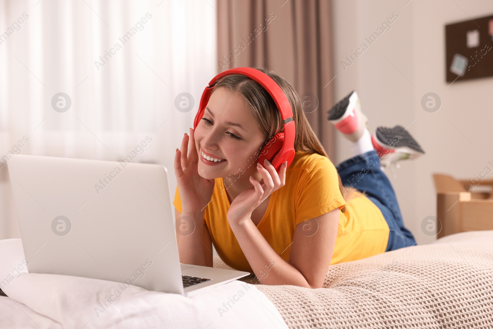 Photo of Online learning. Teenage girl in headphones with laptop on bed at home
