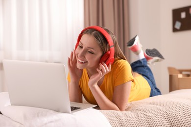 Photo of Online learning. Teenage girl in headphones with laptop on bed at home