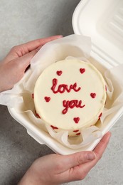 Photo of Woman holding takeaway box with bento cake at light grey table, top view. St. Valentine's day surprise