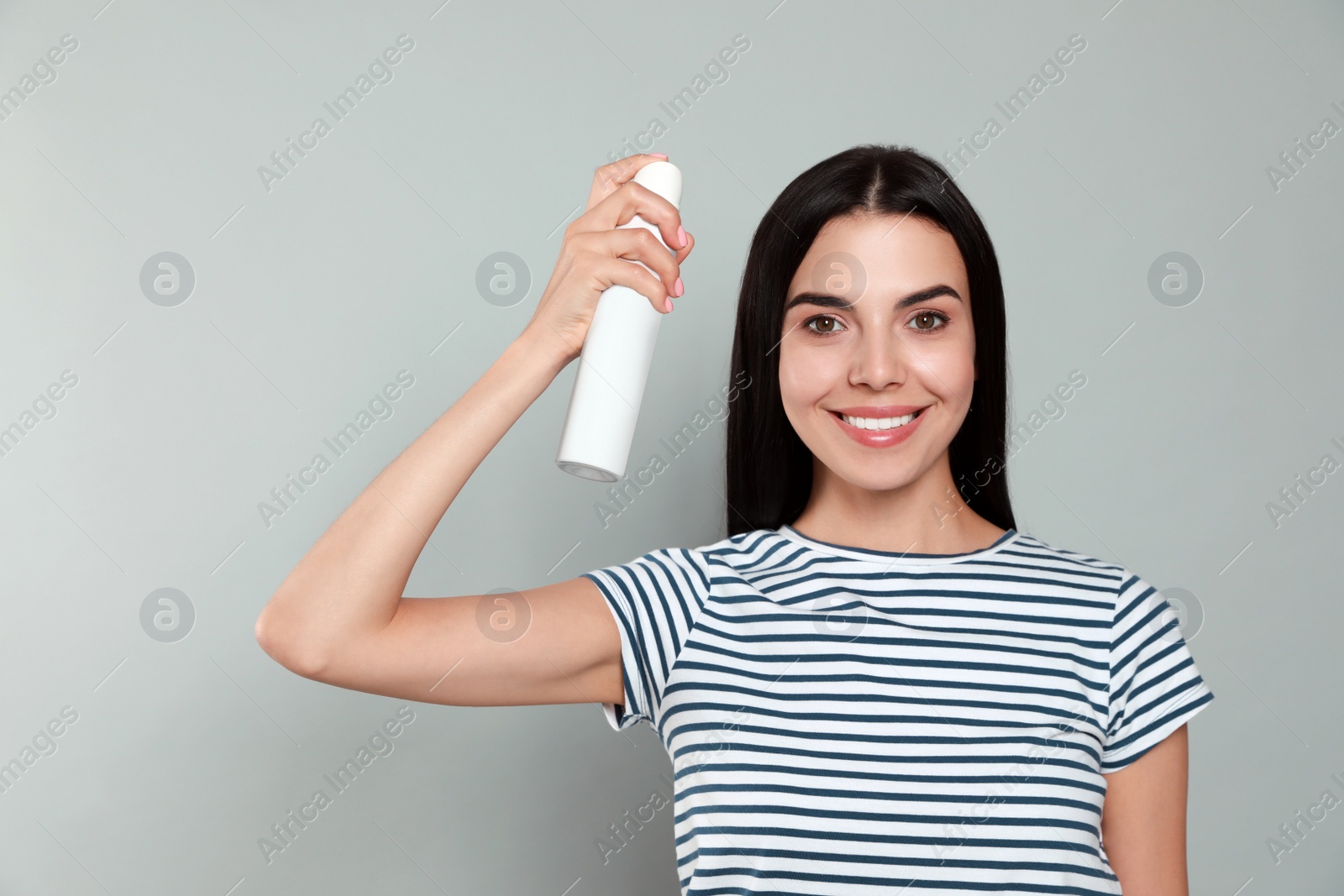 Photo of Woman applying dry shampoo onto her hair on light grey background