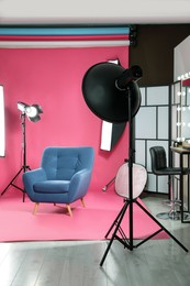 Photo of Stylish blue armchair in photo studio with professional equipment