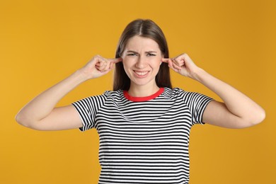 Photo of Emotional young woman covering her ears with fingers on yellow background