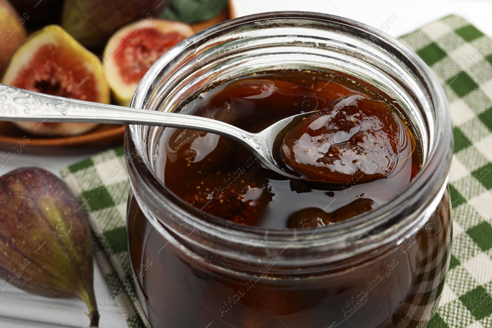 Photo of Jar of tasty sweet fig jam on white table, closeup