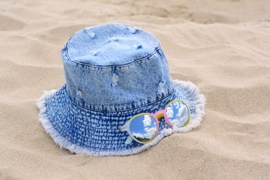 Jeans hat and sunglasses on sand, closeup. Beach accessories