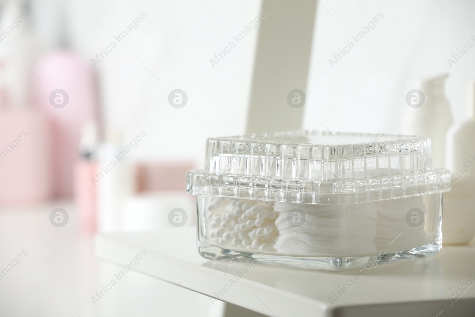 Photo of Container with cotton swabs and pads on white shelf in bathroom, closeup. Space for text