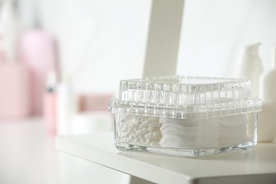 Container with cotton swabs and pads on white shelf in bathroom, closeup. Space for text