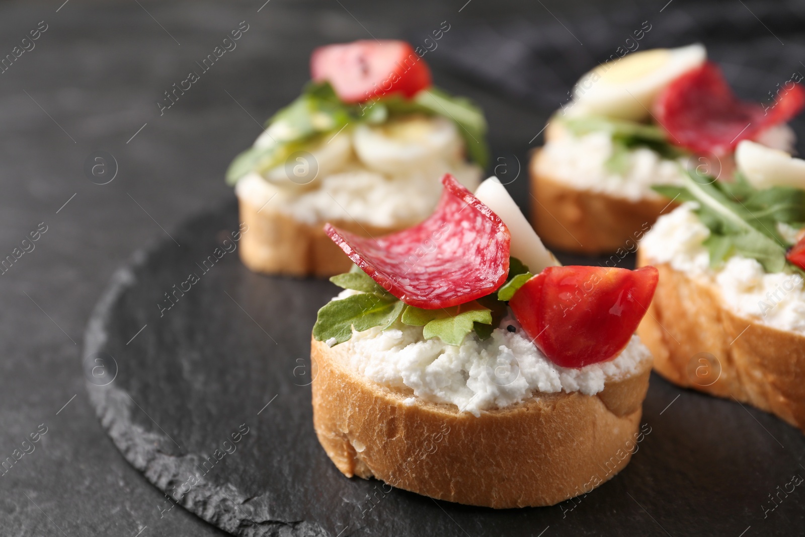 Photo of Delicious bruschettas with sausage and cheese on black table, closeup