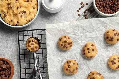 Bowl with dough and uncooked chocolate chip cookies on light grey table, flat lay