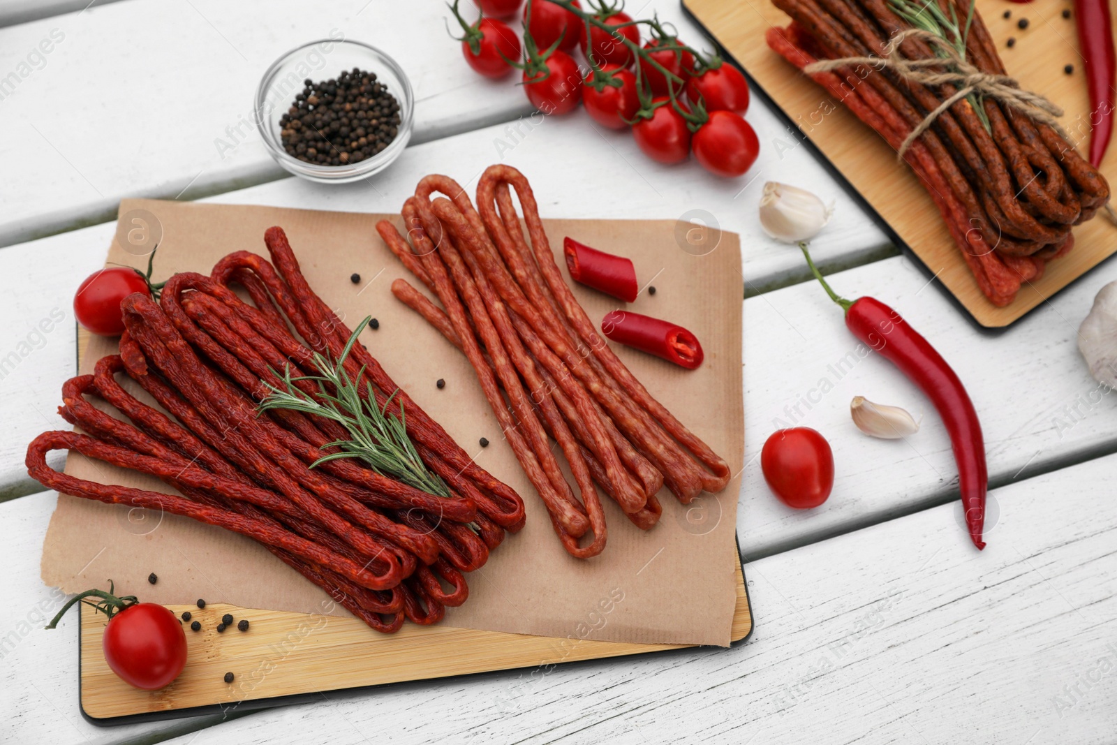 Photo of Delicious kabanosy with rosemary, peppercorn, chilli and tomatoes on white wooden table, above view