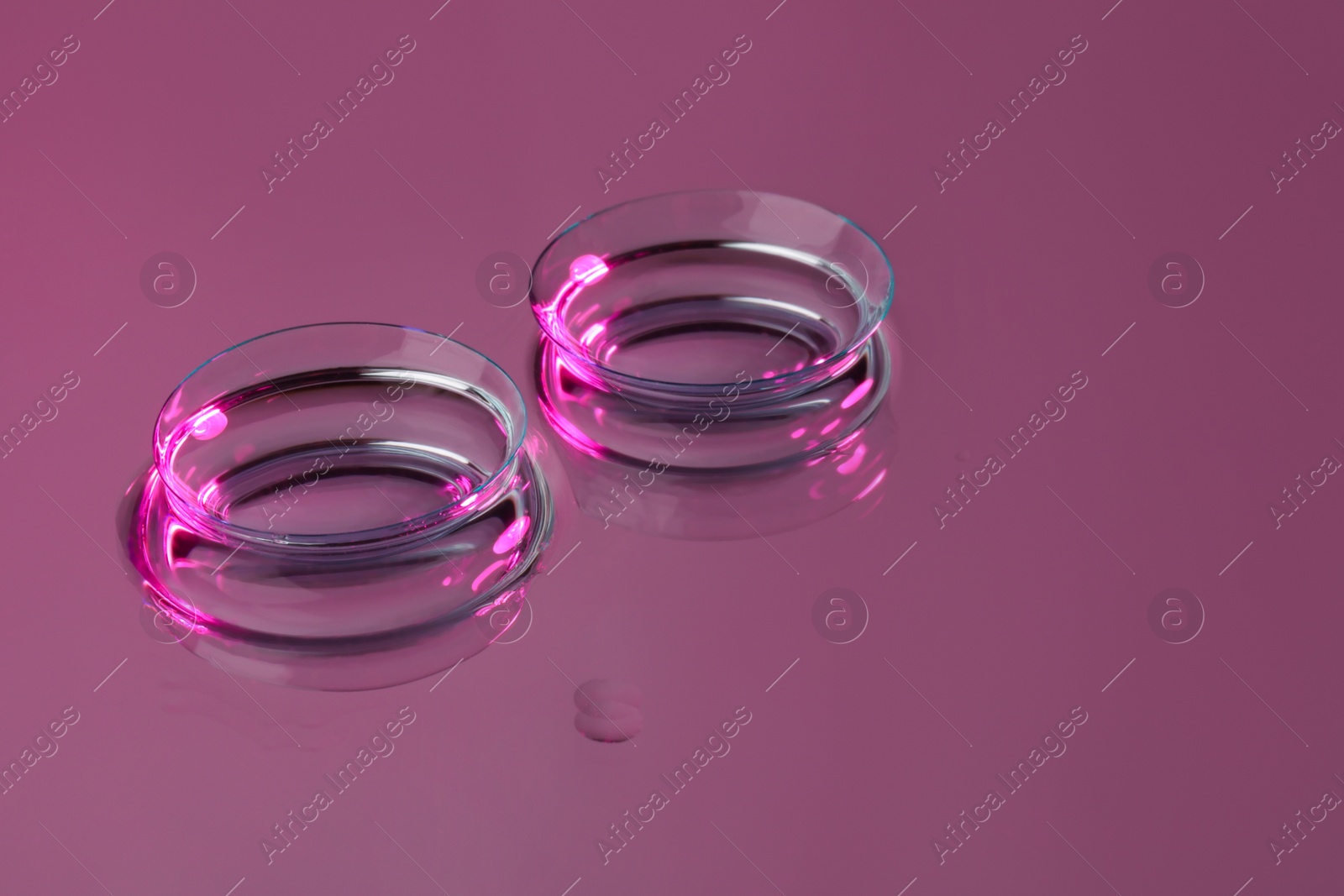 Photo of Pair of contact lenses on pink reflective surface. Space for text