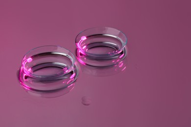 Photo of Pair of contact lenses on pink reflective surface. Space for text