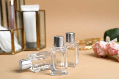 Photo of Perfumes and rose flowers on beige table