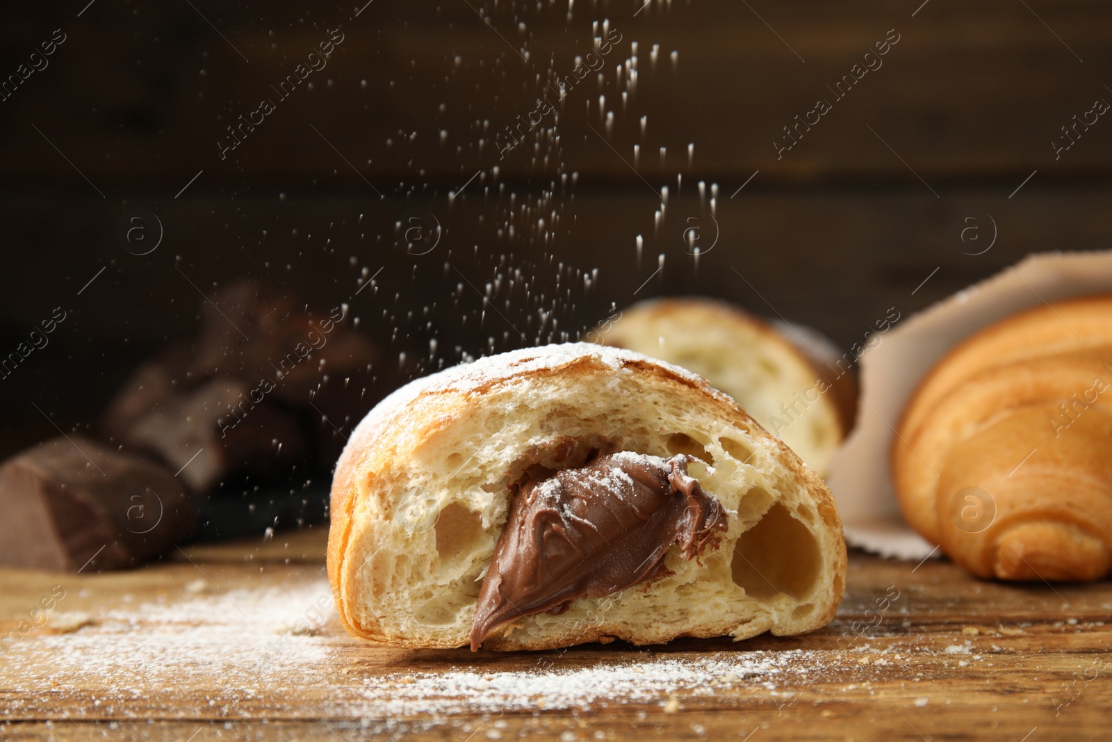 Photo of Sprinkling sugar powder onto tasty croissant with chocolate on wooden table
