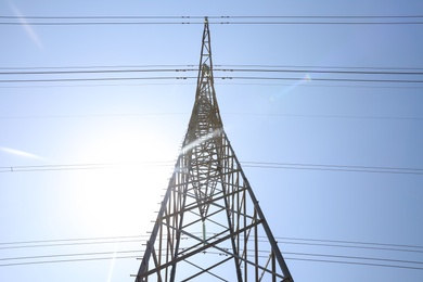 Photo of High voltage tower with electricity transmission power lines against blue sky, low angle view