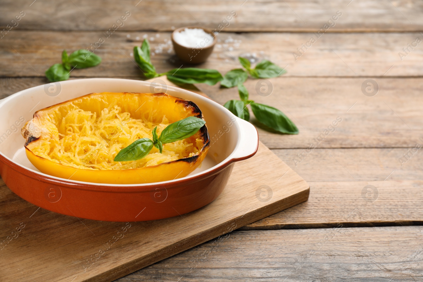 Photo of Half of cooked spaghetti squash with basil in baking dish on wooden table. Space for text