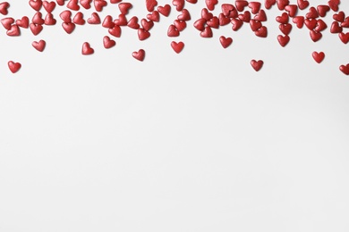 Photo of Bright heart shaped sprinkles on white background, flat lay. Space for text