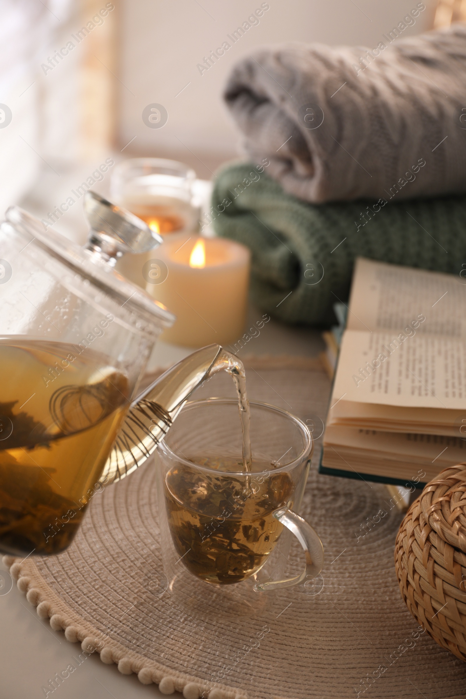 Photo of Pouring freshly brewed tea into cup at table in room, closeup. Cozy home atmosphere