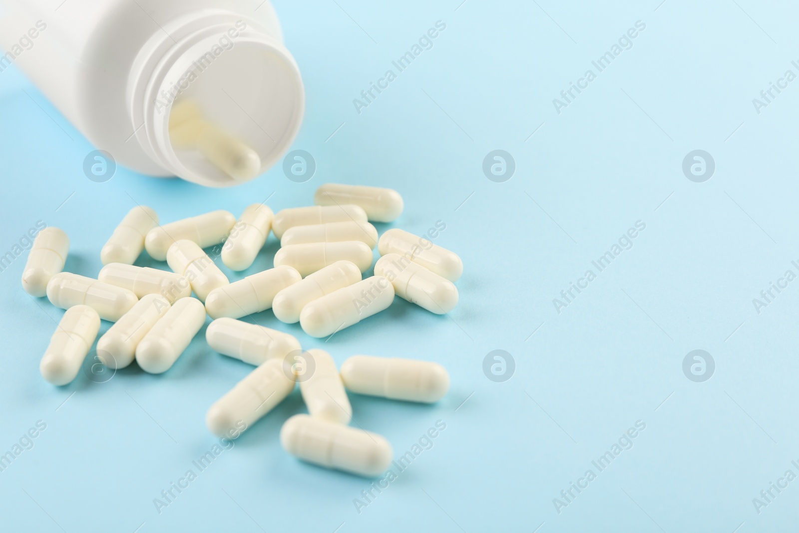 Photo of Bottle and vitamin capsules on light blue background, closeup. Space for text