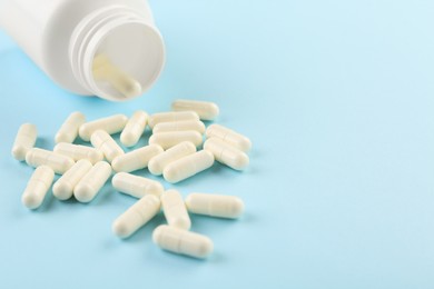 Bottle and vitamin capsules on light blue background, closeup. Space for text