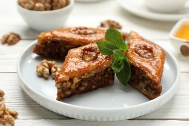 Photo of Delicious sweet baklava with walnuts and mint on white wooden table, closeup