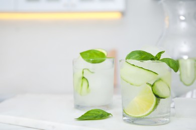 Photo of Tasty fresh cucumber water with sliced lime and basil on white table indoors