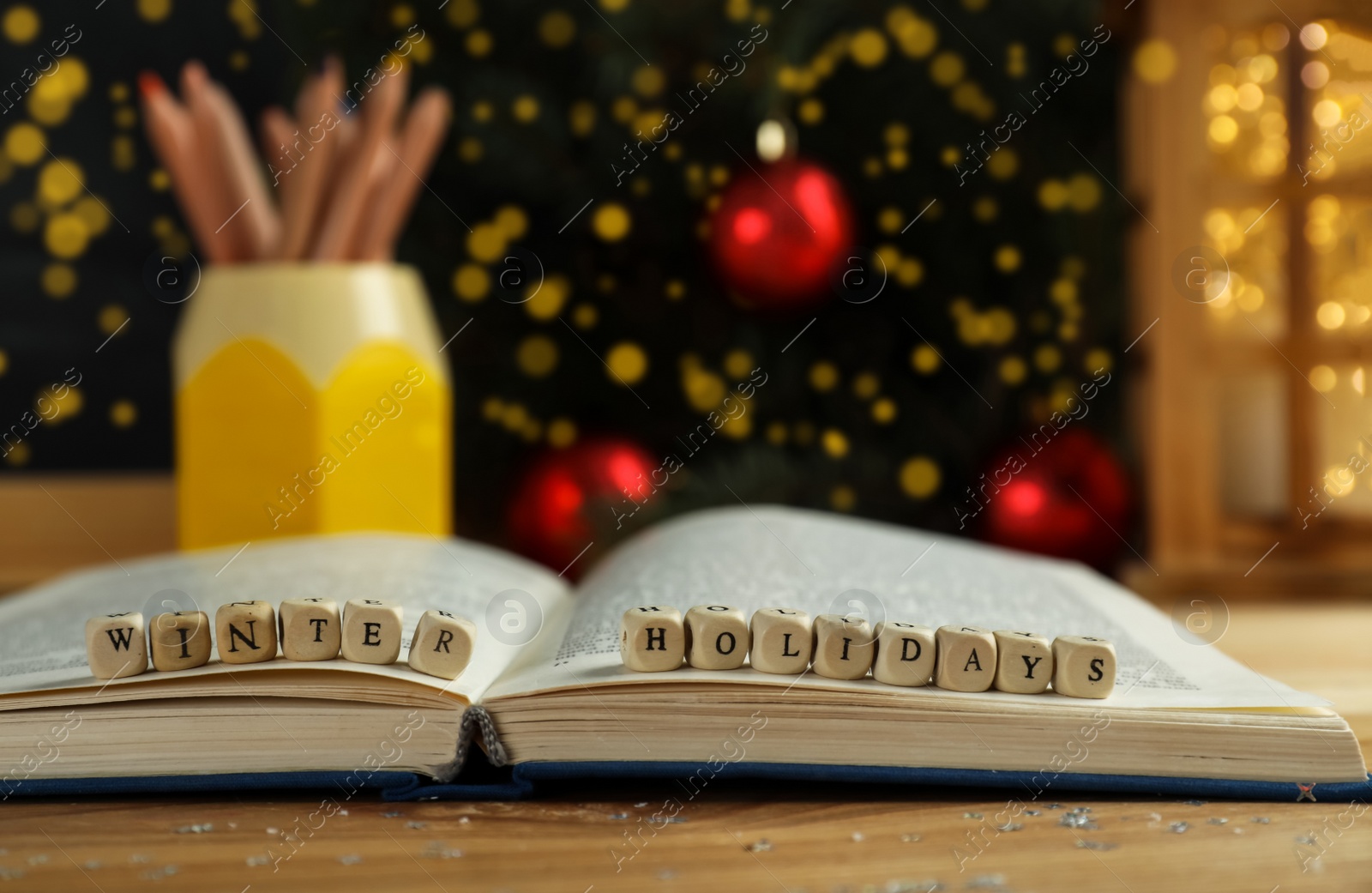 Photo of Wooden cubes with phrase Winter Holidays and open book on table, closeup. Space for text