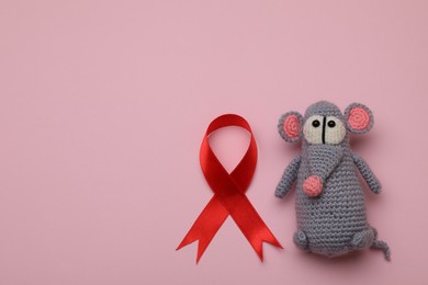 Photo of Cute knitted toy mouse and red ribbon on pink background, flat lay with space for text. AIDS disease awareness