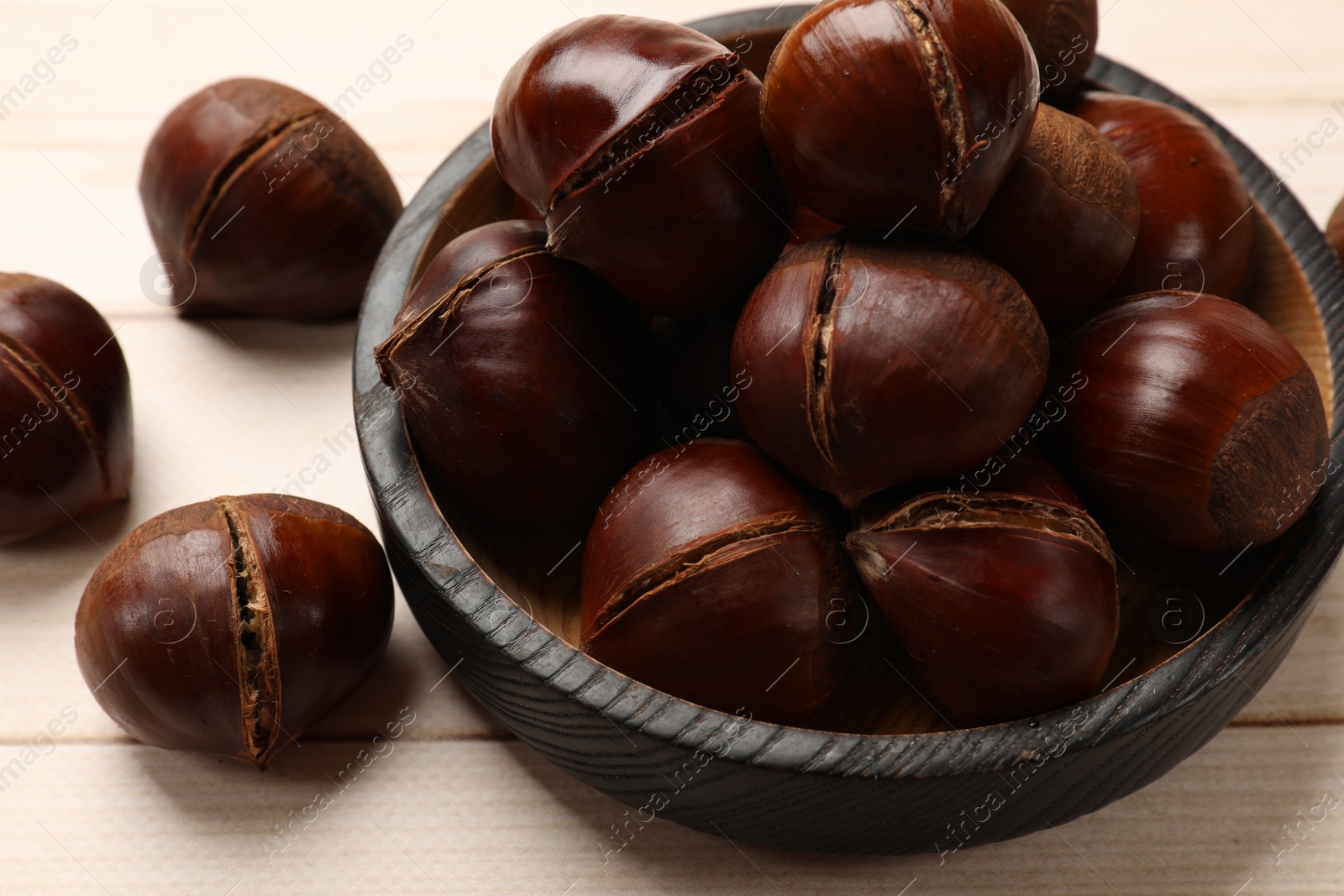 Photo of Plate with roasted edible sweet chestnuts on wooden table, closeup