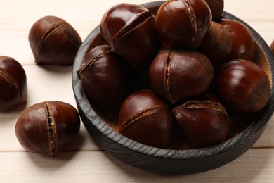 Photo of Plate with roasted edible sweet chestnuts on wooden table, closeup