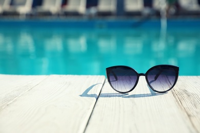 Sunglasses near swimming pool on sunny day. Space for text