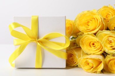 Beautiful bouquet of yellow roses and gift box on white background, closeup