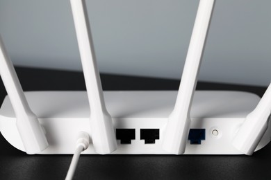 Photo of New white Wi-Fi router on black table, back view